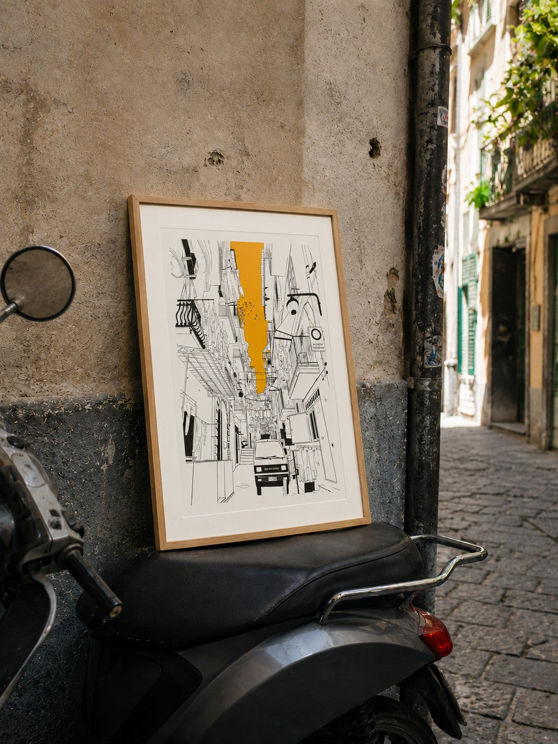 Framed Naples alleyway print leaning against a wall on a parked scooter in an Italian street
