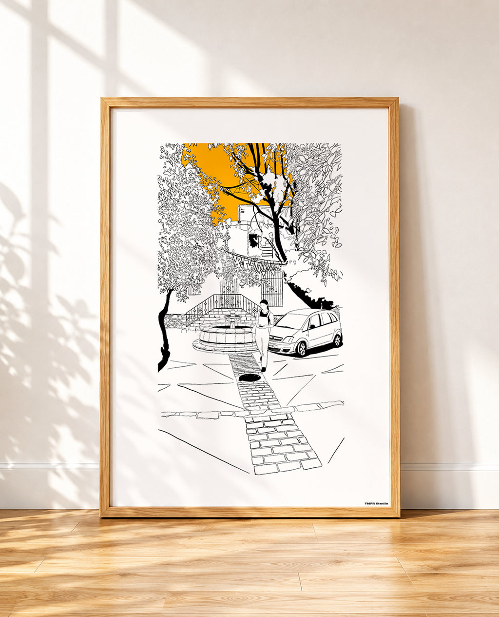 framed Black and white line drawing of a cobblestone street scene with a stone fountain, a woman walking, a parked car and overhanging trees, with a bright orange sky breaking through the branches