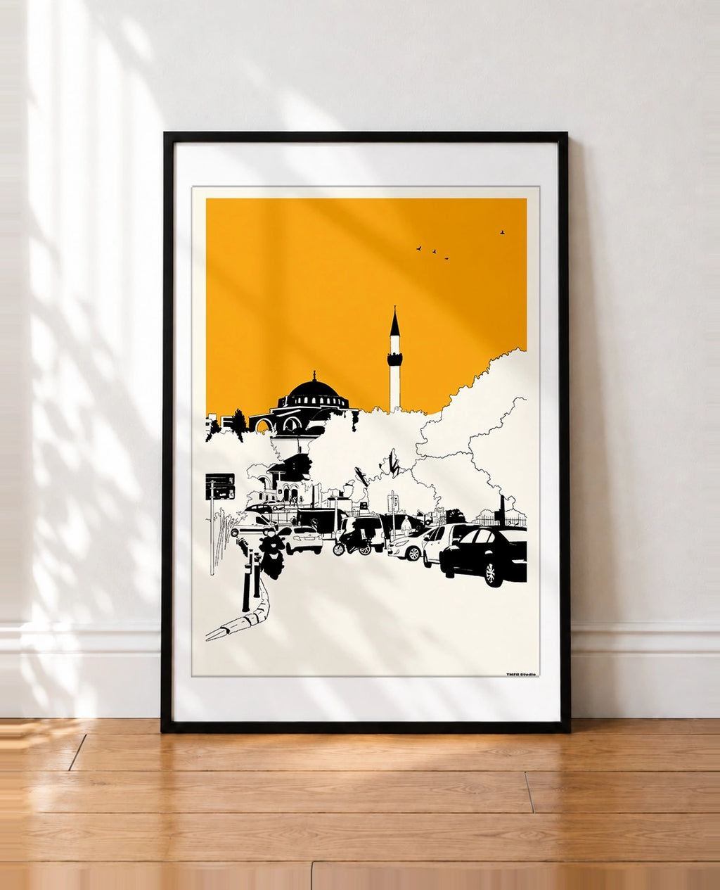 Black framed Istanbul mosque and minaret print with an orange sky leaning against a wall
