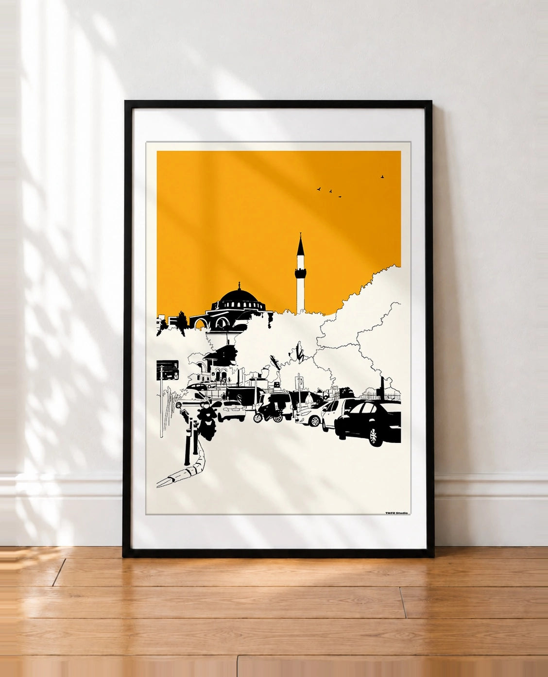 Black framed Istanbul mosque and minaret print with an orange sky leaning against a wall
