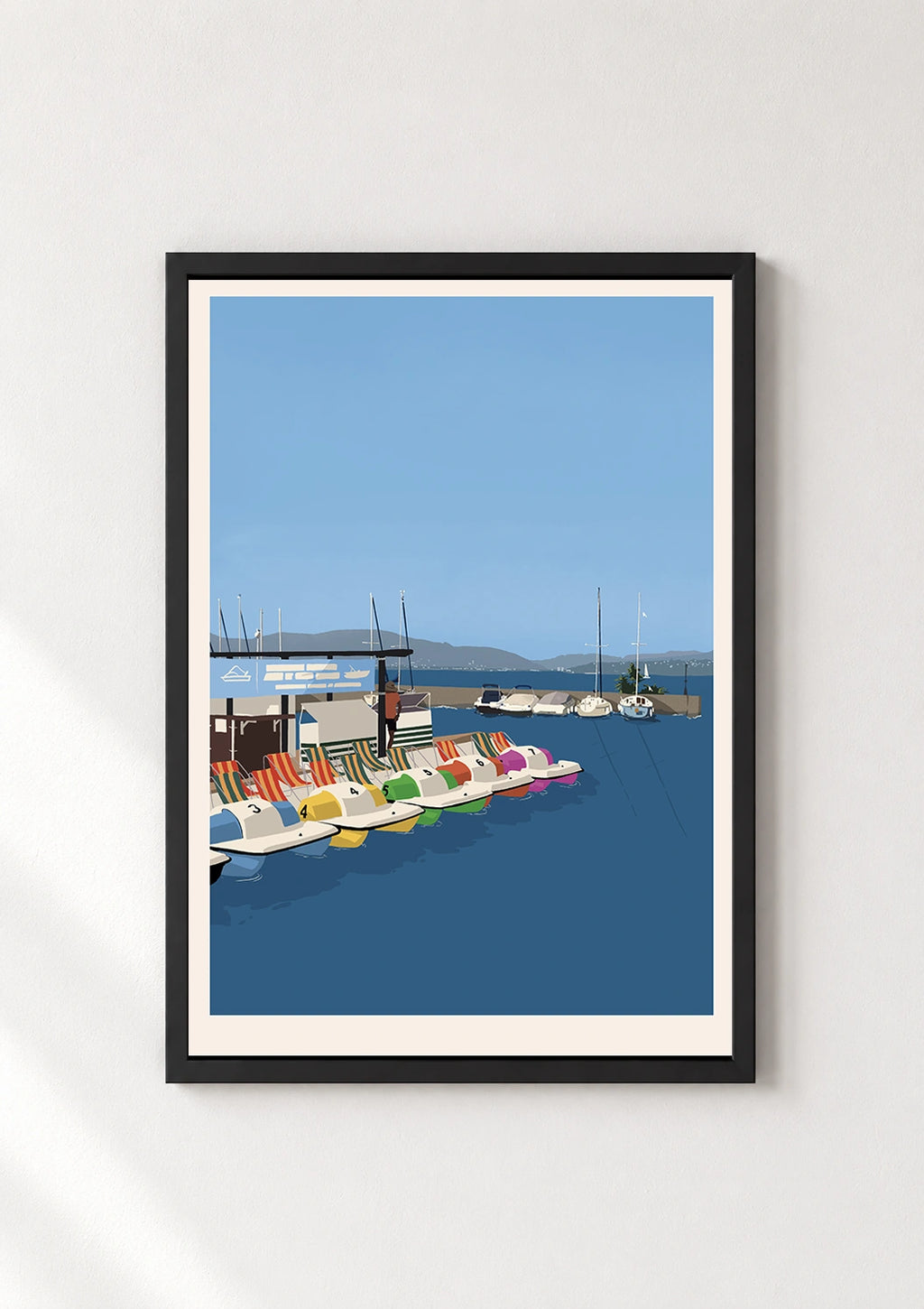 Black framed print of colorful pedal boats docked on a lake with sailboats and mountains
