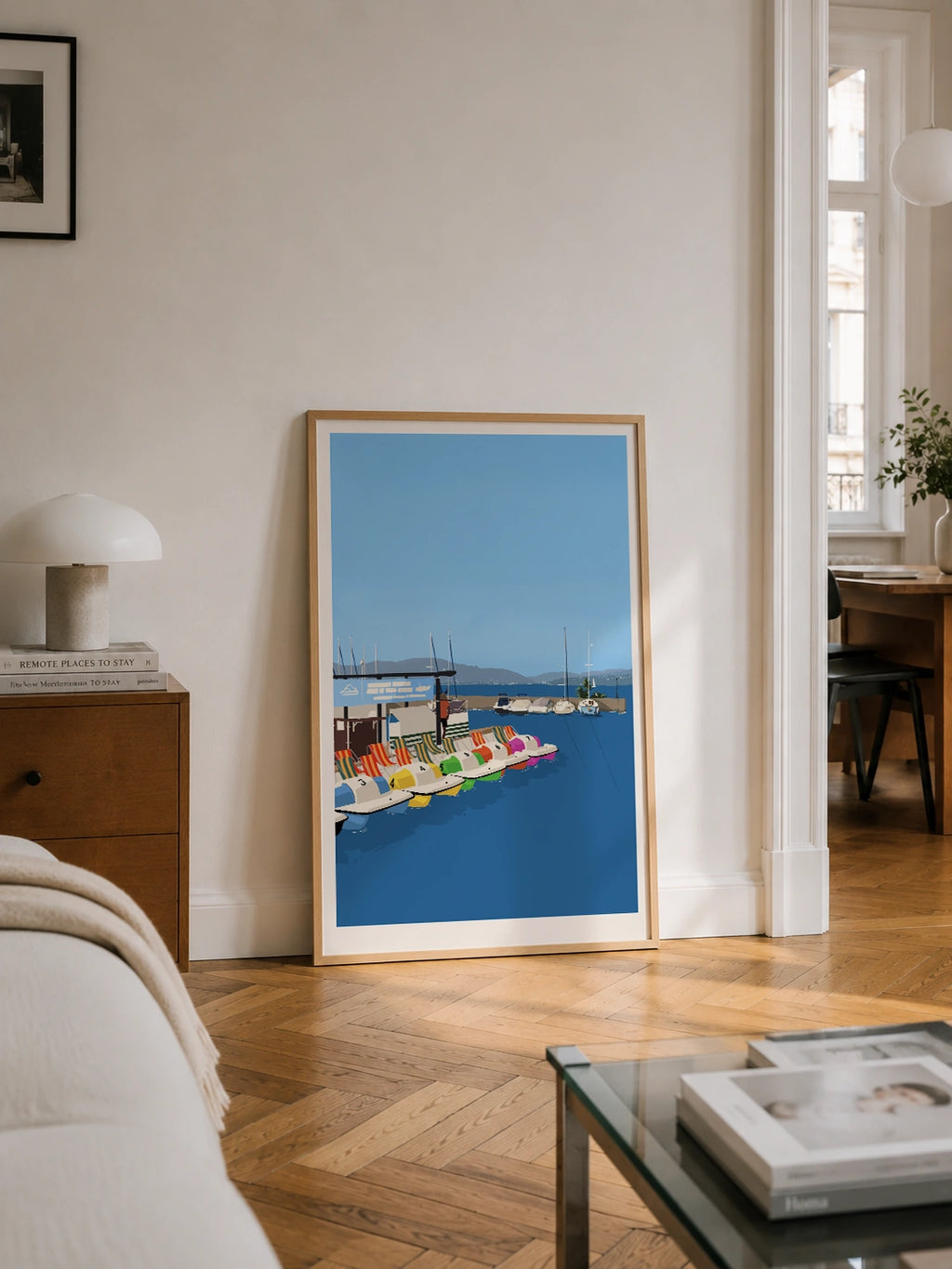 Colorful pedal boats lake print leaning against a wall in a bedroom with herringbone flooring
