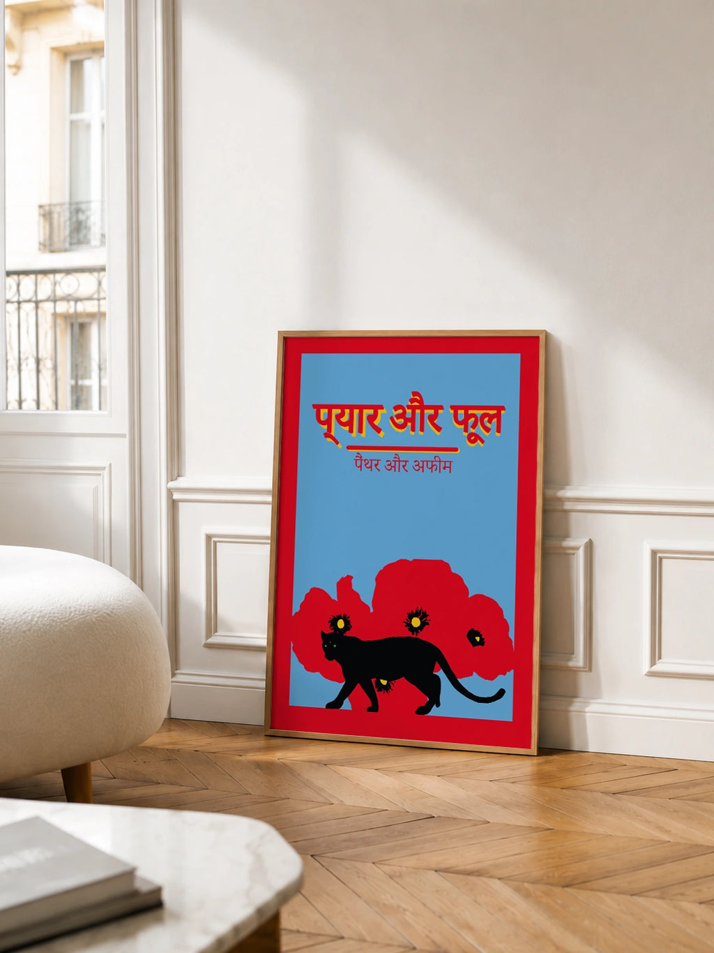 love and flower poster leaning against a wall in a Parisian-style room with chevron parquet flooring, wainscoting and a boucle ottoman, near tall windows with a wrought-iron balcony
