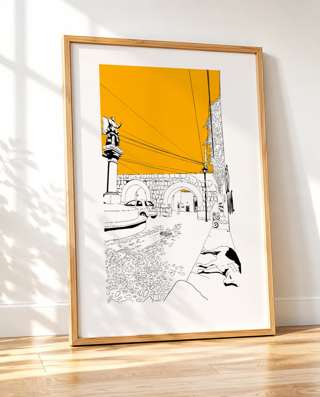 Framed black and white line-art poster leaning against a wall on a wooden floor, with natural light and tree shadows falling across the frame
