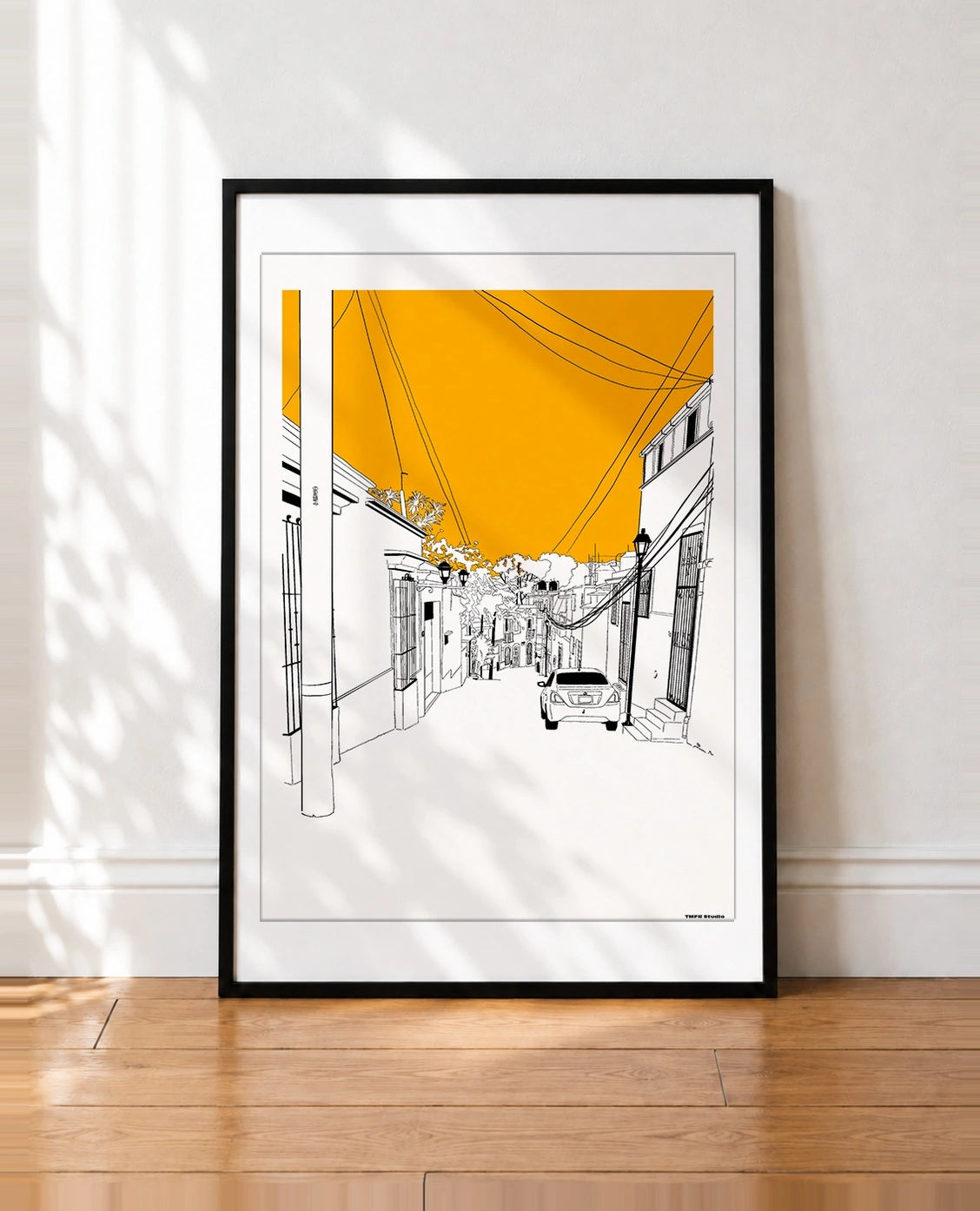 framed Illustration of a narrow Oaxaca street with white colonial buildings, power lines, a parked car, and an orange sky
