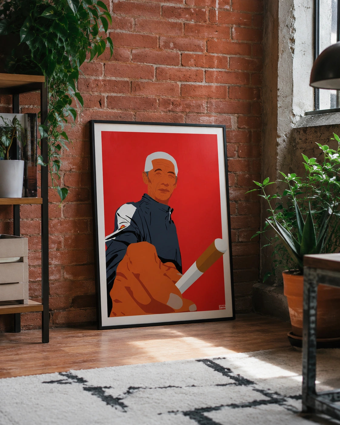 Framed Old Man Cigarette poster leaning against an exposed brick wall in a loft, surrounded by potted plants, a Moroccan-style rug and warm natural light
