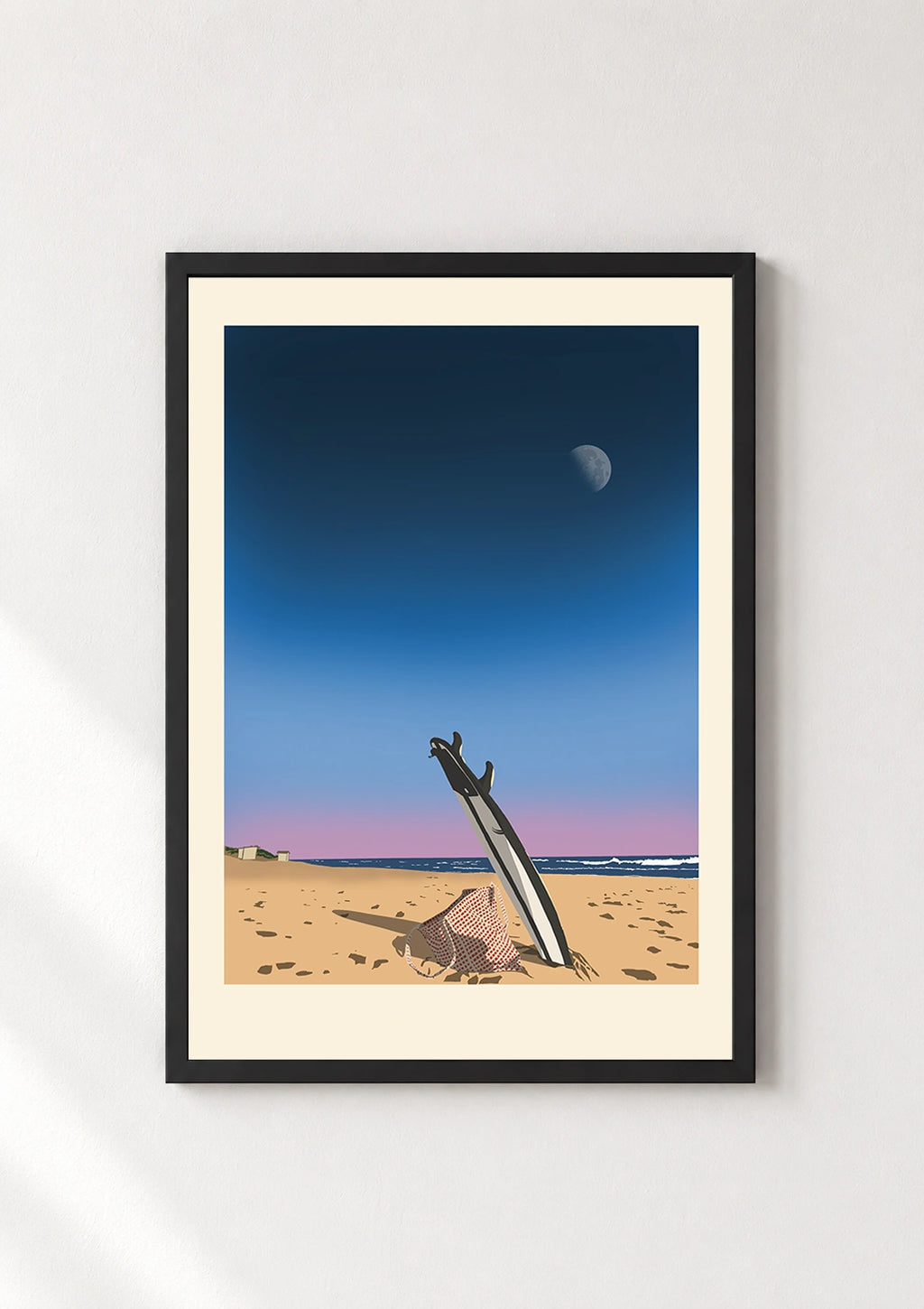 Black framed print of a surfboard standing in sand at dusk with the moon and ocean in the background
