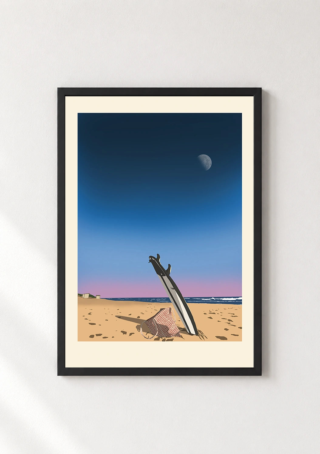 Black framed print of a surfboard standing in sand at dusk with the moon and ocean in the background
