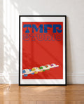 A framed art print leaning against a white wall on a wooden floor. The print features a bold red background with the words 'TMFR STUDIO' in blue retro lettering at the top and a row of colorful cartoon-style characters in a boat at the bottom.