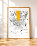 A framed art print featuring a black and white sketch of a city street in Naples with a bold yellow vertical highlight, displayed in a light wood frame against a white wall on a wooden floor.