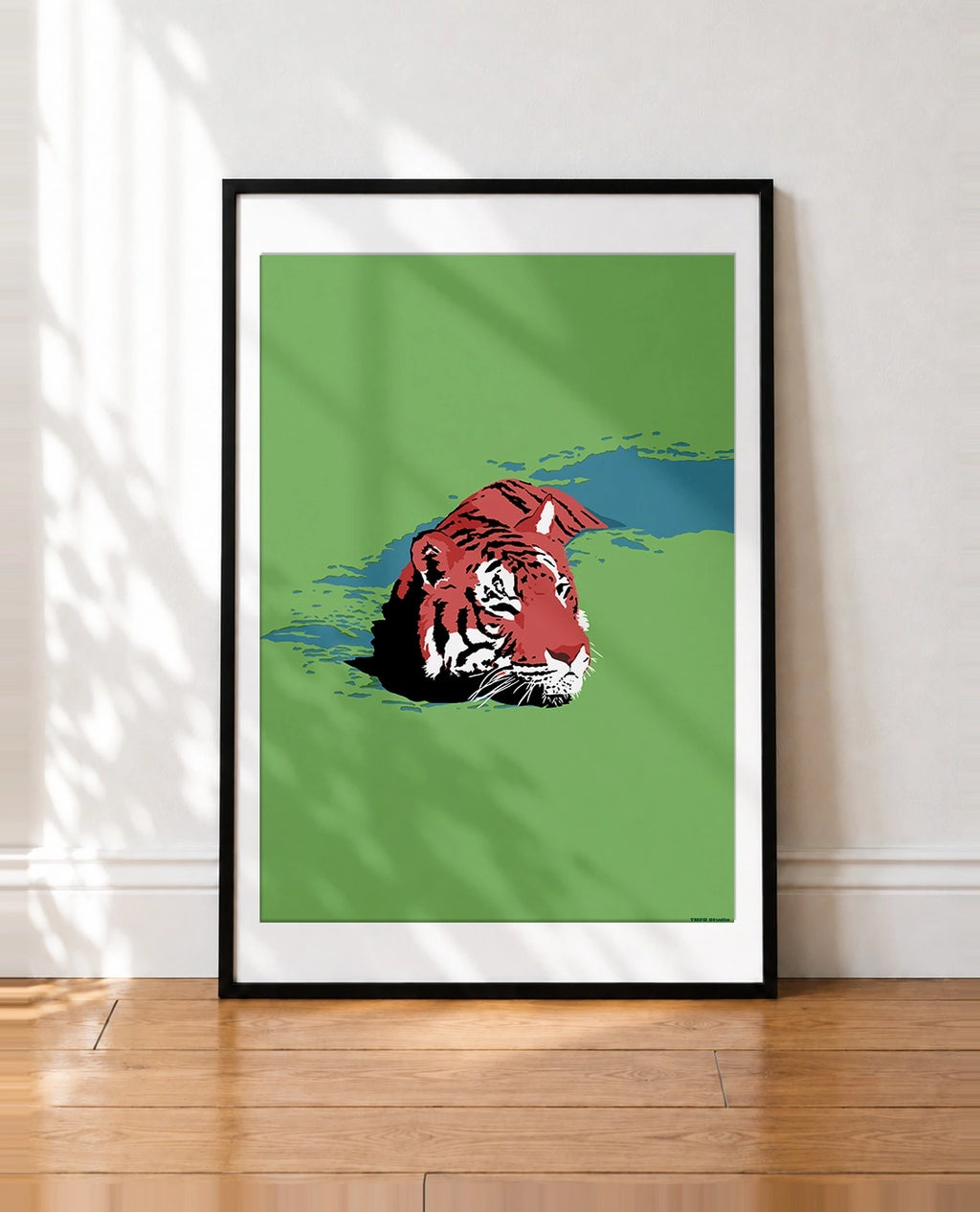 A framed art print featuring a stylized red and black tiger head on a green background, leaning against a white wall on a wooden floor with soft shadow overlays.
