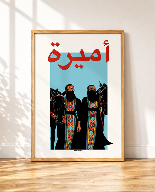 A framed art print leaning against a white wall on a wooden floor. The print features a light blue background with bold red Arabic calligraphy at the top and a stylized illustration of two figures in black traditional robes with colorful patterned borders, flanked by black horses.